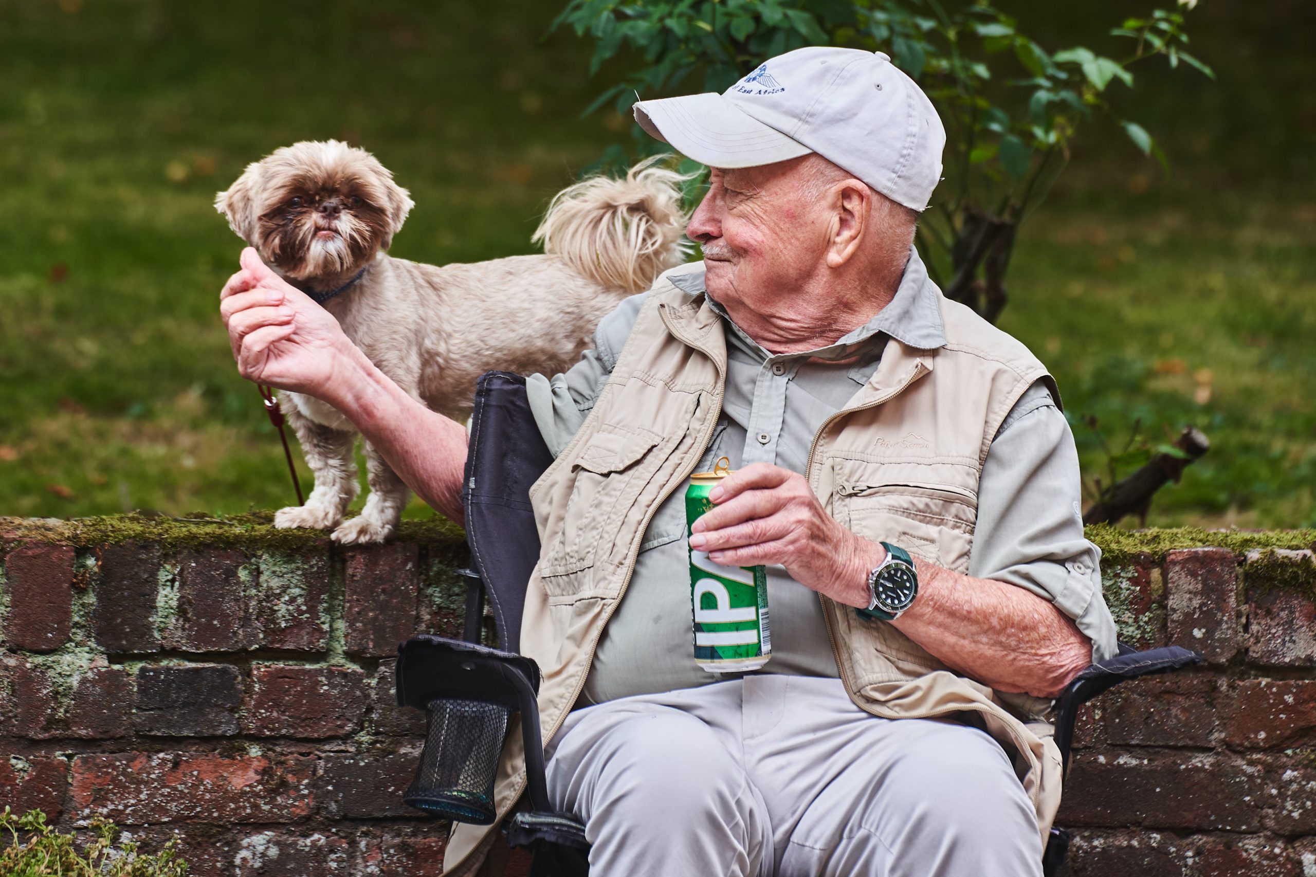 MNan sitting on a bench with a drink in one hand and stroking a dog with the other