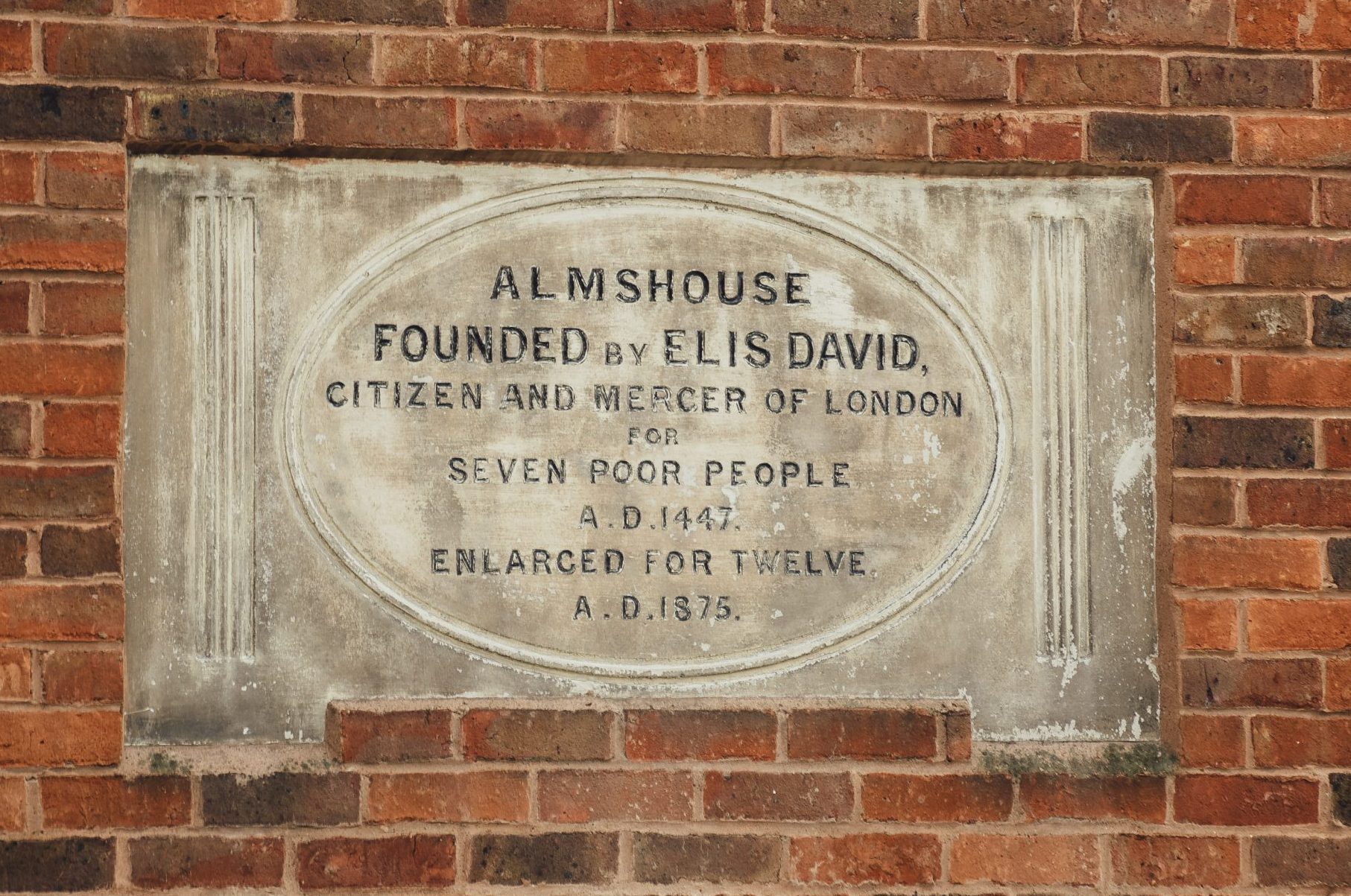 Plaque on wall that reads: Almshouse founded by Elis David, citizen and mercer of London for seven poor people A.D. 1447. Enlarged for twelve A.D. 1875
